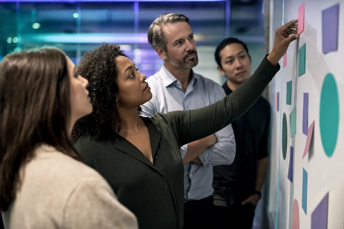 A team at a whiteboard wall weighing team role cards together, one person placing a card