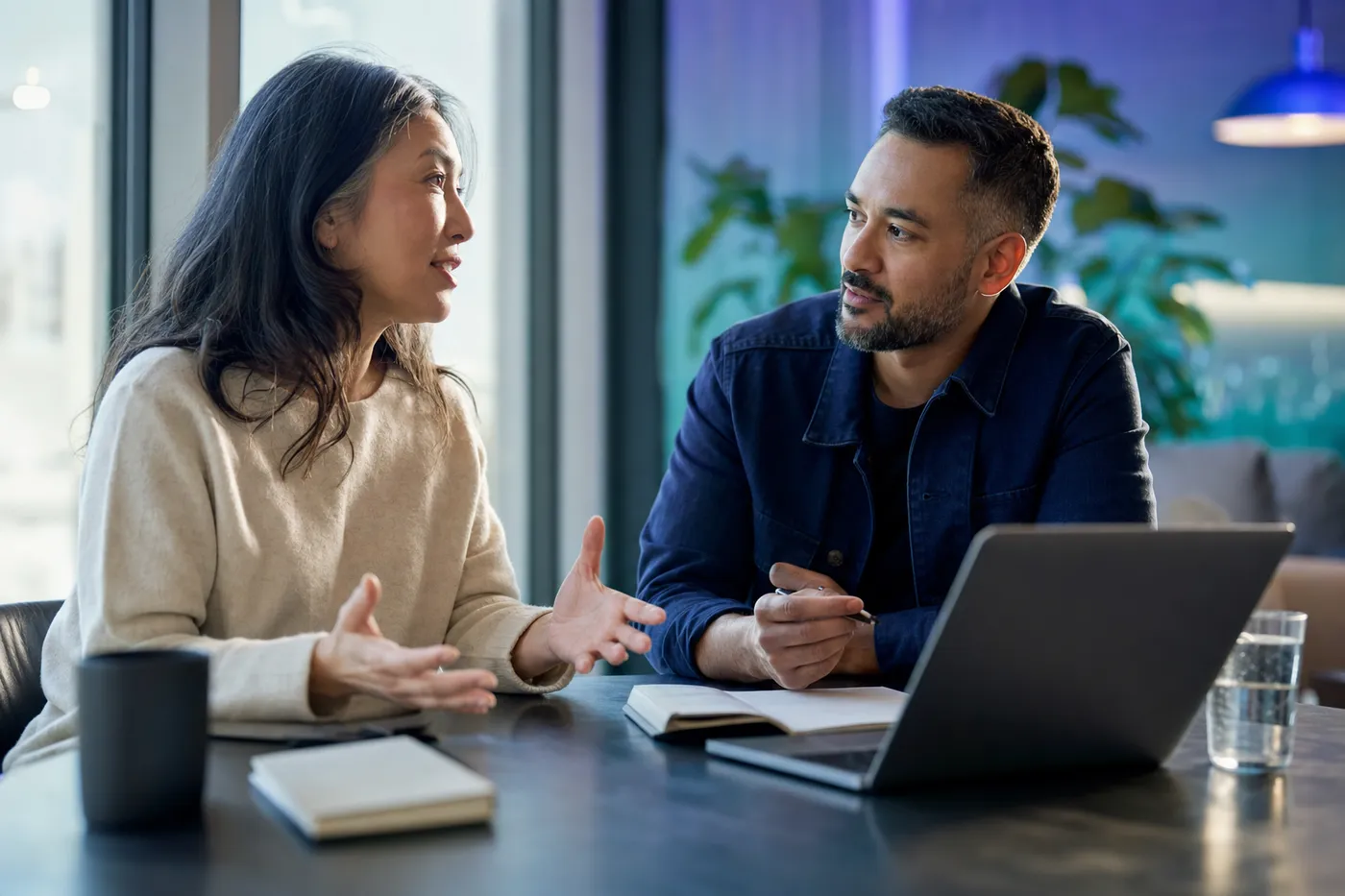Two colleagues in a calm one-on-one working session at a window table, one listening intently
