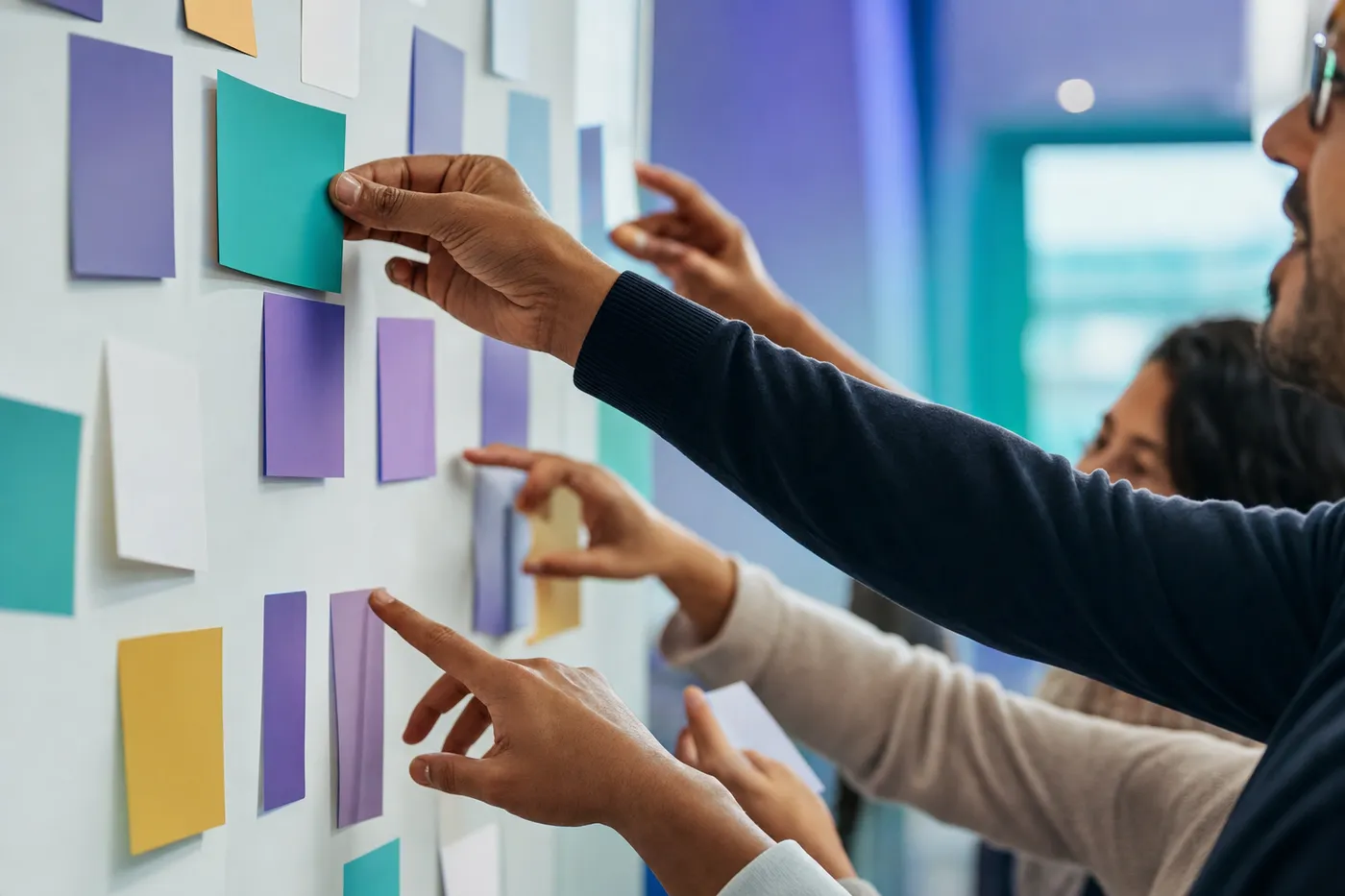 Hands arranging colored cards on a wall during a team workshop